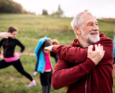 A large group of fit and active people doing exercise in nature, stretching.