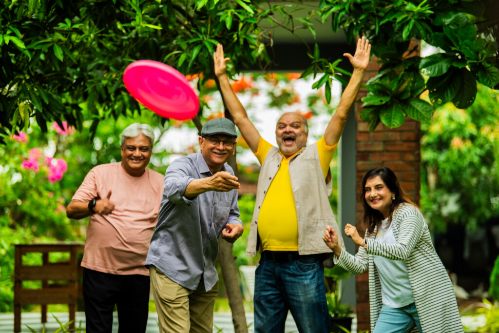 Senior friends enjoying throwing frisbee in garden during reunion, smiling and playing together