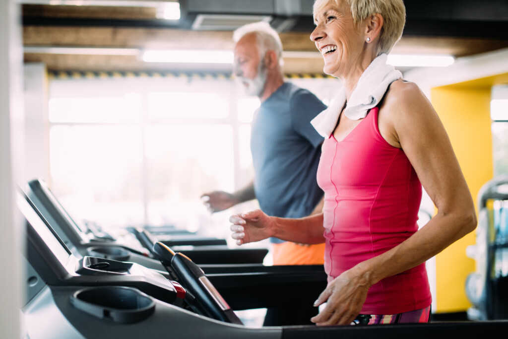Happy mature people running together on treadmills in gym.
